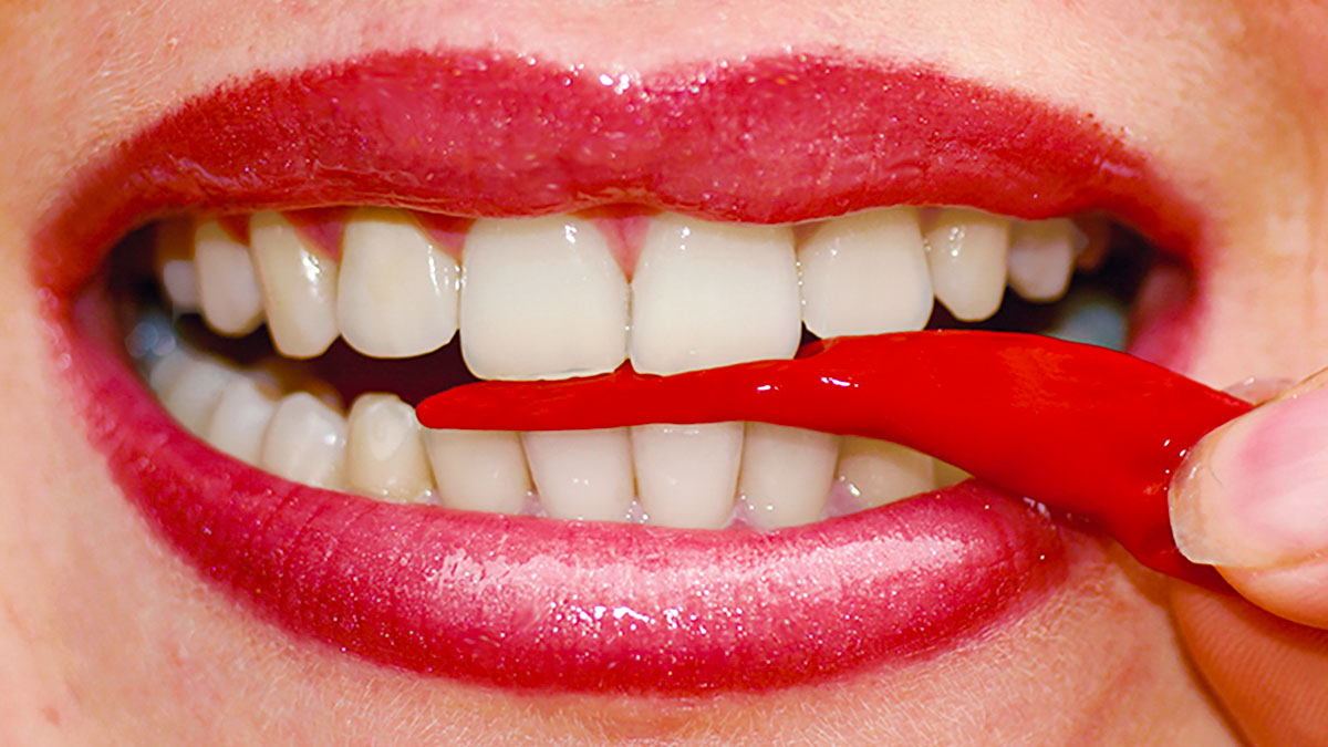 Frau mit schönen Zähnen beißt auf eine rote Peperoni